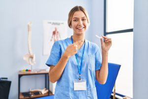 Young blonde woman holding plastic aligner for bruxism smiling happy pointing with hand and finger