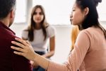 Diverse young people sitting in circle receiving support during a therapy session. Millennial female teenager calming depressed partner in professional guidance meeting - Depression treatment concept