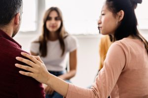 Diverse young people sitting in circle receiving support during a therapy session. Millennial female teenager calming depressed partner in professional guidance meeting - Depression treatment concept