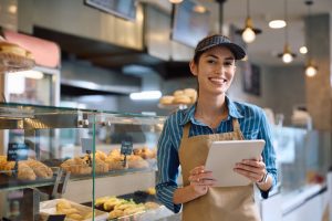 Happy female bakery worker using touchpad and looking at camera.
