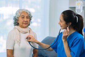 Senior Asian female patient listening to doctor using stethoscope in hospital. Doctor in uniform using stethoscope to examine heart. Senior woman.